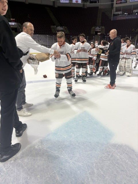 A coach congratulates a Compuware player skating past the trophy line